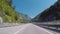 View on a highway from the car moving to Olympic village against blue sky, trees and Caucasian mountains in summer