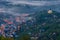 View from hill with forest meadow on town Banska Stiavnica with street lights on and fog and mist in valley