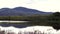 View of a hill on the Isle of Skye with a small loch in the foreground. In the center is a road where an unrecognizable car passes