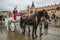 A view of a horse drawn carriage riding past the Adam Mickiewicz Monument and Cloth Hall in the medieval old town square in Krakow