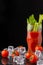 View of ice cubes with cherry tomatoes, glass glass with Bloody Mary cocktail and celery, on black background, vertical,