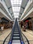 View inside modern shopping mall with escalator and bright light from windows in ceiling