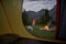 View from inside tent at sunset. Alone tourist, hiker standing at bonfire