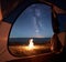 View from inside tourist tent. Night camping near seacoast. Campfire under night sky full of stars