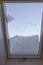 View of interior of snow-covered dormer window on roof of house from room covered with snow on frosty winter day.