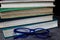 View on isolated stack of old yellowed books on wood table with blue reading glasses