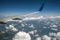 View of jet airplane wing from inside flying over white puffy clouds in blue sky. Travel and air transportation concept