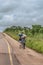 View of kids walks with head load, along roadside, tropical landscape as background