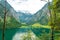 View of Konigssee upper lake with clear green water, reflection, mountains, sky background and pier Salet Alm, Bavaria, Germany
