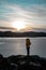 View of a lake on a sunny evening in Norway with a woman in yellow parka in the front looking at the lake.