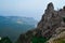 view of large stone rock among green trees stands on cliff against backdrop of Black sea coast in Crimea