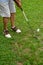 View of legs with shorts of man with golf shoes hitting a white ball, on green grass, in portrait