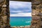 View of Ligurian sea water, rock cliff of Palmaria island and boat through brick stone wall window, Portovenere