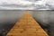 View of a long wooden pier leading out into clear ocean waters with sailboats behind