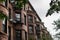 View looking down a row of old brownstone apartment buildings with half round fronts, metal balconies and oxidized gutters