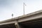 View looking up at concrete highway bridge, supports and beams, street lights