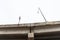 View looking up at the concrete supports of an elevated roadway bridge with light stanchion and sign post