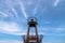 View looking up at a weathered steel light house tower at the end of a pier with blue sky and bright white feathery clouds in the