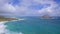 View of Makapuu beach. Waves of Pacific Ocean wash over yellow sand of tropical beach. Magnificent mountains of Hawaiian