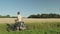 View of male with bicycle going along rye field. Rye field merging with blue sky and green trees