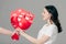 View of man gifting bouquet of red paper cut cards with hearts symbols to pretty girl isolated on grey