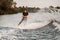 View of man in wetsuit holds cable in his hands and wakeboarding on splashing wave