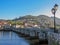 View on medieval bridge through river and small mountain town with red tailed roofs, countryside Portugal