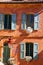 View on mediterranean bright facade of red ochre house with blue window shutters, green doors, flower pots