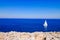 View on the Mediterranean Sea with rocks in the front and a sailboat on the right side