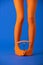 View of model in bright orange tights holding fork and sausage with legs on blue