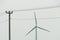 view of a modern windmill against a blue sky. The white blades of the wind turbine. Renewable energy source. Old power lines next