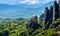 View of monastery of St Nicholaos Anapafsas on top of sedimentary pillar and green hills of Meteora valley at midday