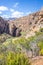 View of a Mountain range with large red rocky outcrops covered with lush green vegetation, Montagu Springs