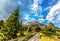 View of the mountains of the Rosengarten group Rosengarten with meadows and fir trees, a road and a mountain hut under a blue cl