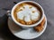 View of a mug of a cappuccino coffee with fluffy, white milk froth on the table covered with neutral grey tablecloth in front of