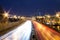 View of multilane urban highway with glowing lines of light from car headlamps and modern architecture