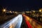 View of multilane urban highway with glowing lines of light from car headlamps and modern architecture