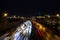 View of multilane urban highway with glowing lines of light from car headlamps and modern architecture