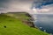 View on the Mykines island with moody clouds covering the top of the mountains and sheep grazing on the pasture, Mykines island,