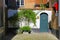 View on narrow front yard of medieval house with green tree, water pump blue door