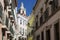 View of a narrow street and buildings with a tower of the Sao Vincente de Fora church on the backrgound, in the historic neighbour