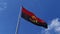 View of the national flag of the Republic of Angola isolated against a blue sky with few clouds, fluttering in the wind