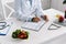 View of nutritionist writing in notebook near vegetables and apple