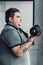 View of Obese tattooed man exercising with dumbbells at sports center