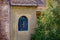 View of an old brick building with an arched window and tiled roof. The plastered facade of the house. Picturesque green tree in