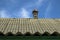 View of old wavy slate roof with moss against blue sky. Texture of old slate with moss. Shed roof covered with old asbestos sheets