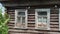 view of an old wooden village house. two broken glass windows. tree branch with green leaves