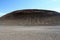 View over barren plain with nothing than small stones on bleak black hill with furrows contrasting with cloudless blue sky