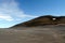 View over barren waste land on black hill with  white spot of melted snow contrasting with blue sky, Iceland