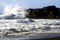 View over black lava sand beach and white furious foaming water surf on wave which breaks against rock